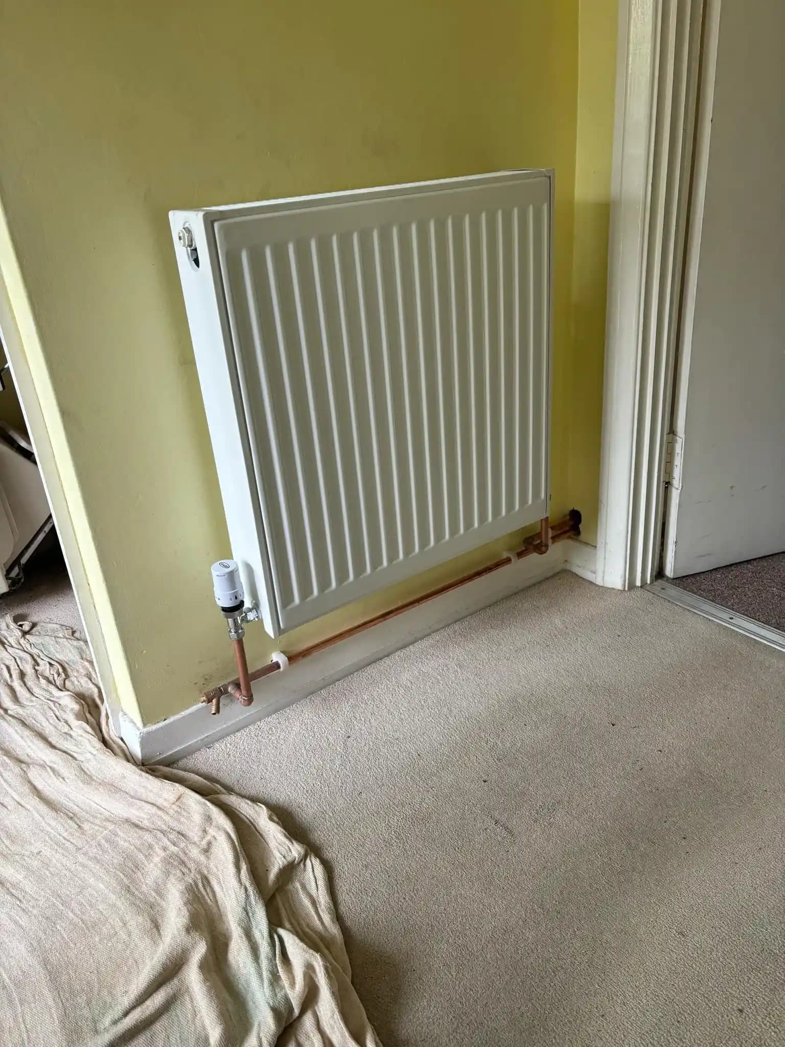 White panel radiator installed in a room with copper pipework.