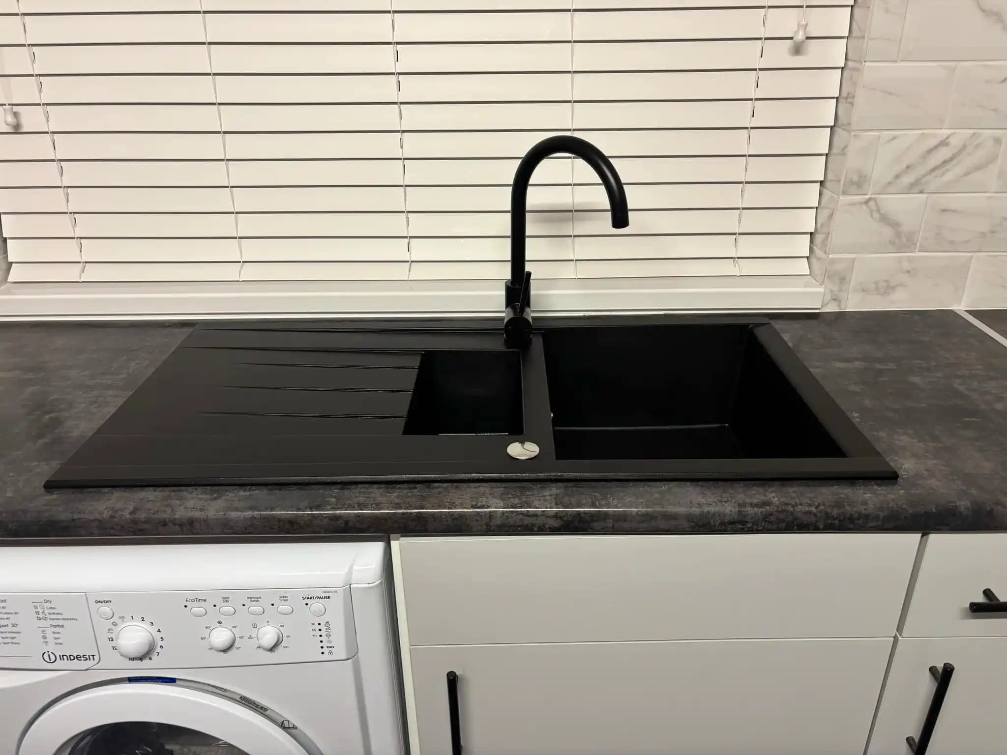 Black kitchen sink and tap installation on a dark worktop.