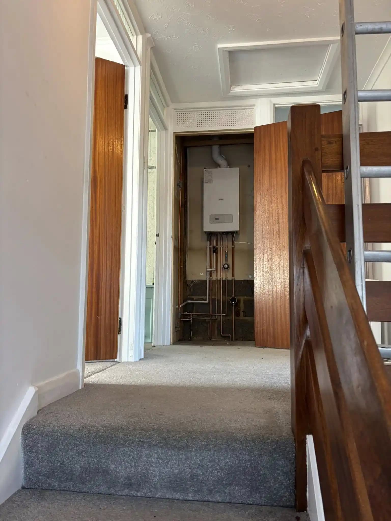 Boiler installed in a hallway cupboard with exposed copper pipework.